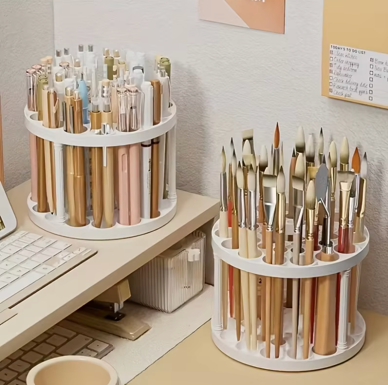 Two 360° rotating brush holders in white filled with art brushes, pens, and makeup tools on a desk.
