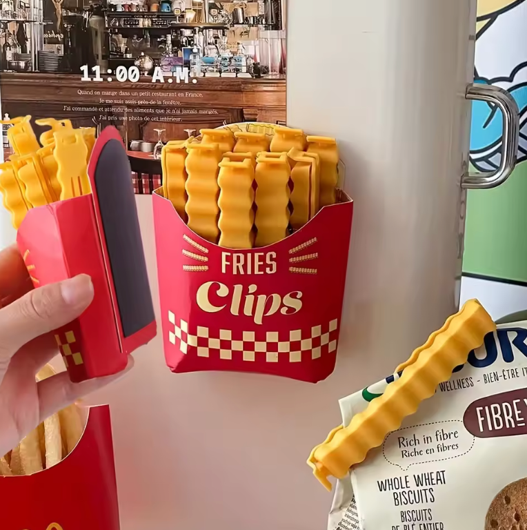 Red container resembling a French fry box holding yellow bag clips, with snacks visible in the background.