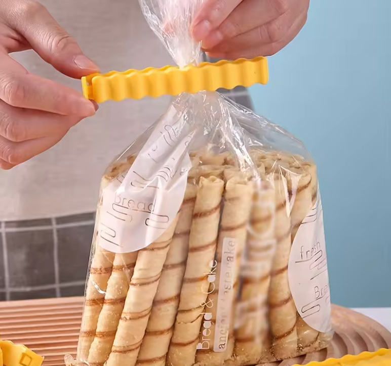 Person sealing a bag of rolled snacks with a yellow French Fry Bag Clip against a light blue background.