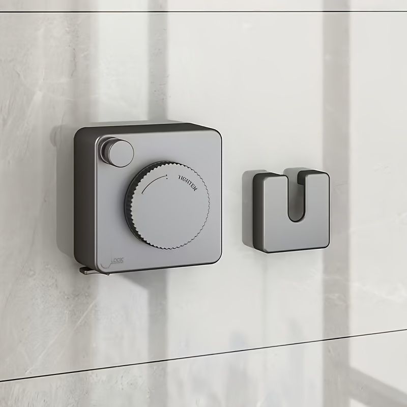 Wall-mounted clothes hanging line installed on a smooth surface with a round dial and hook in neutral gray tones.